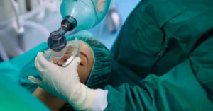Medical professional in surgical attire administering anesthesia to a patient with an oxygen mask, illustrating a safe and comfortable sedation dentistry procedure.