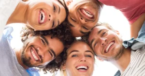 Group of diverse, smiling friends looking down at the camera, representing happiness, relaxation, and confidence — an ideal outcome of quality sedation dentistry and oral care.